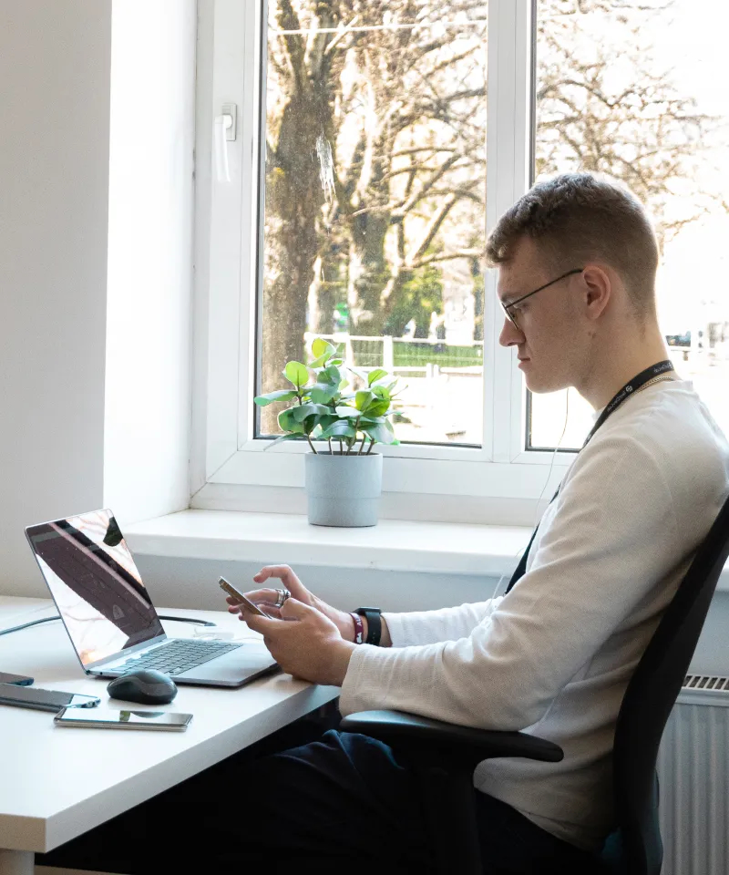 Tillgänglighets-QA-ingenjör sitter vid skrivbordet och använder en mobil enhet.