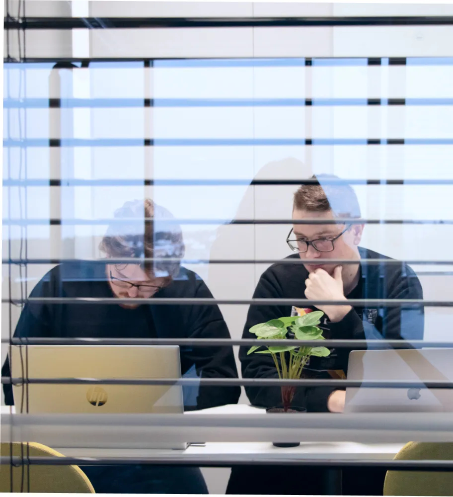 Dos ingenieros de QA sentados en el escritorio y discutiendo actualizaciones del proyecto.