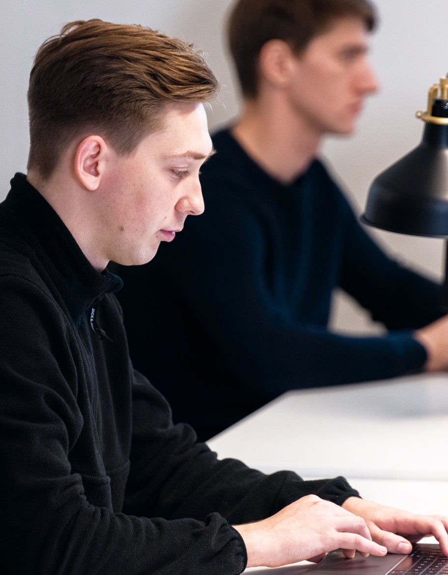 Two engineers, one in the foreground and one in the background working on their projects.